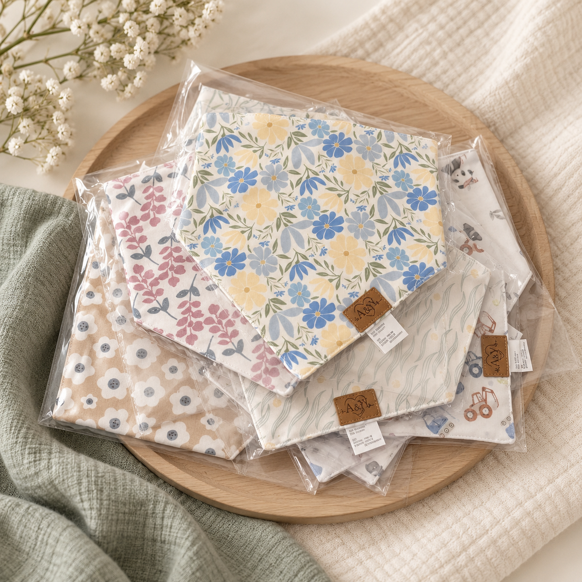 Packaged MINUS bandana bibs on a wooden tray, with Blooming Flowers in the foreground.