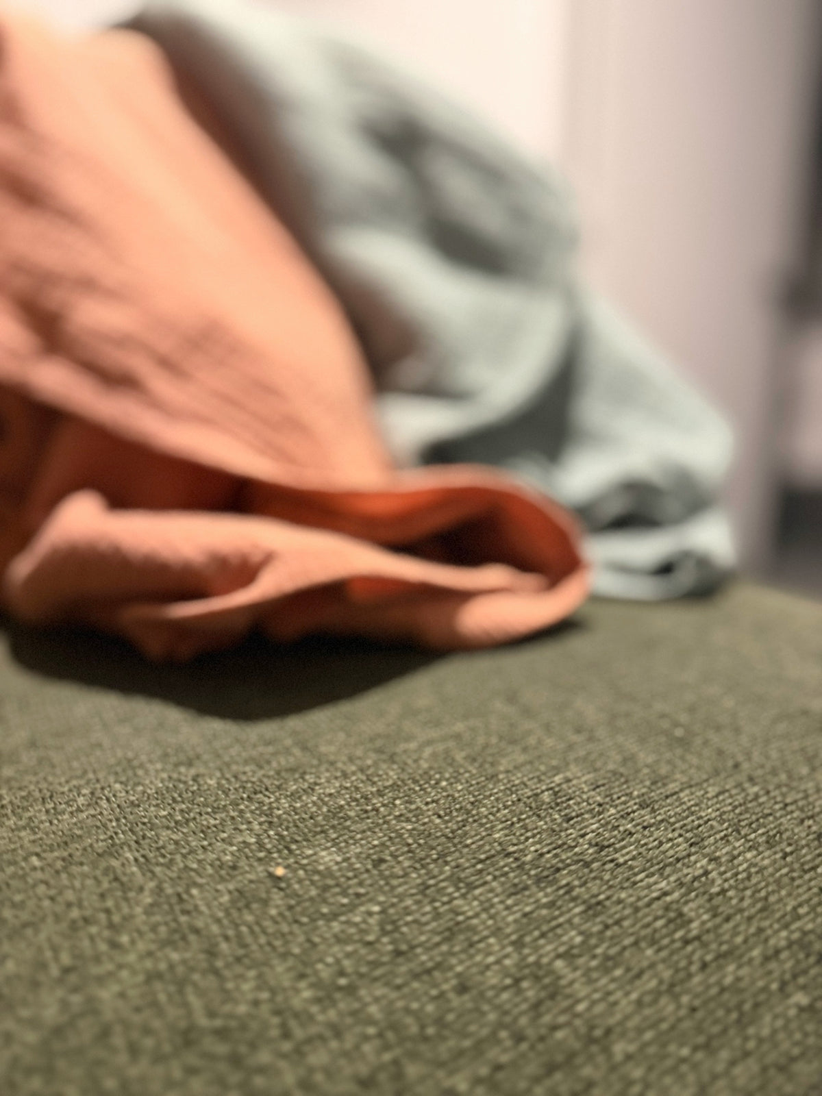 Vue d’ambiance des couvertures en mousseline terracotta et bleu-gris sur un support vert.