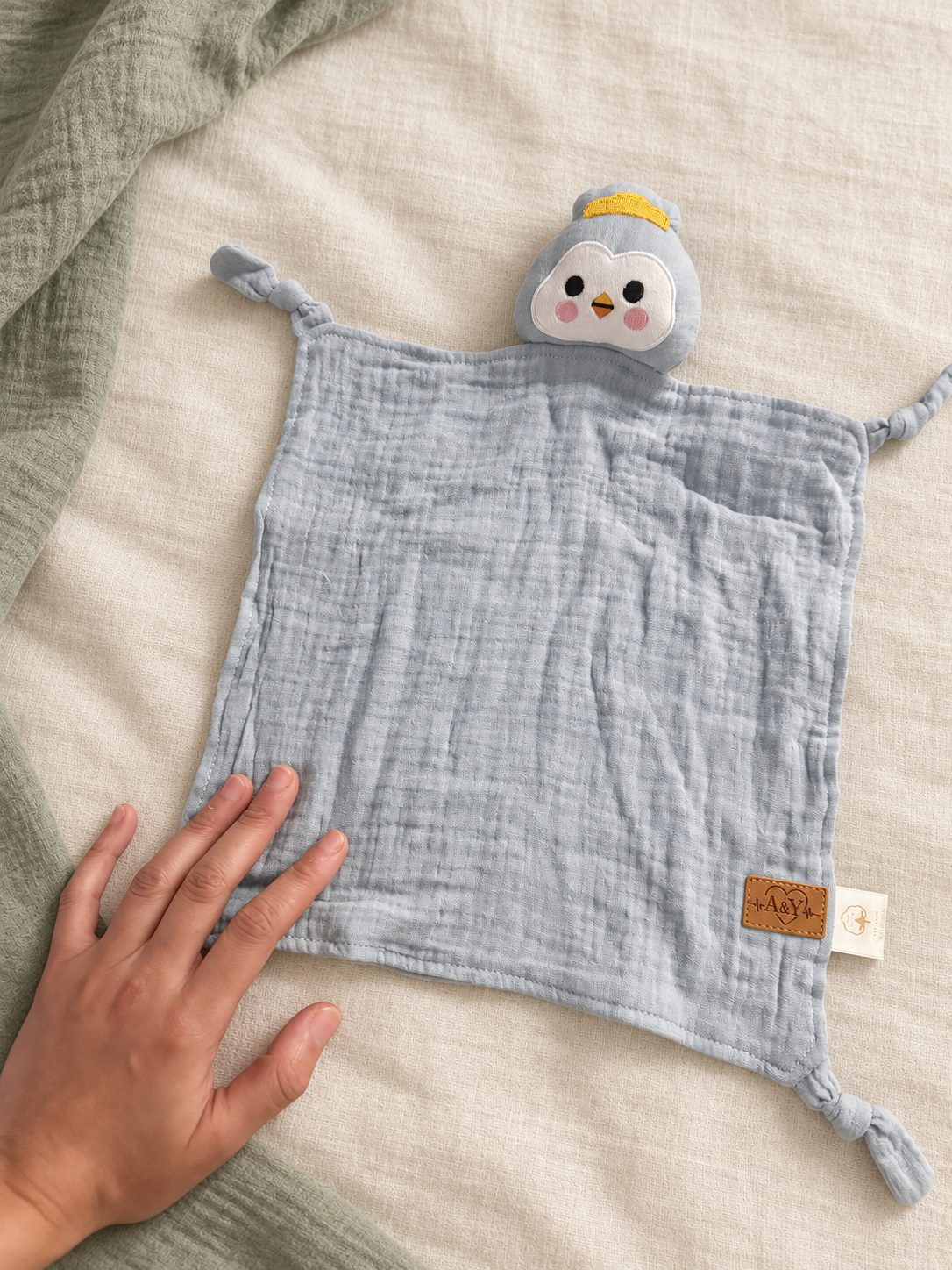 Doudou MINUS pingouin bleu-gris touché par une main adulte pour montrer son format.