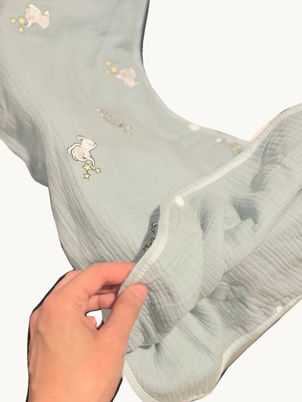 Détail de la gigoteuse verte à éléphants ouverte sur le côté, avec ses boutons-pression et la texture du tissu visibles.