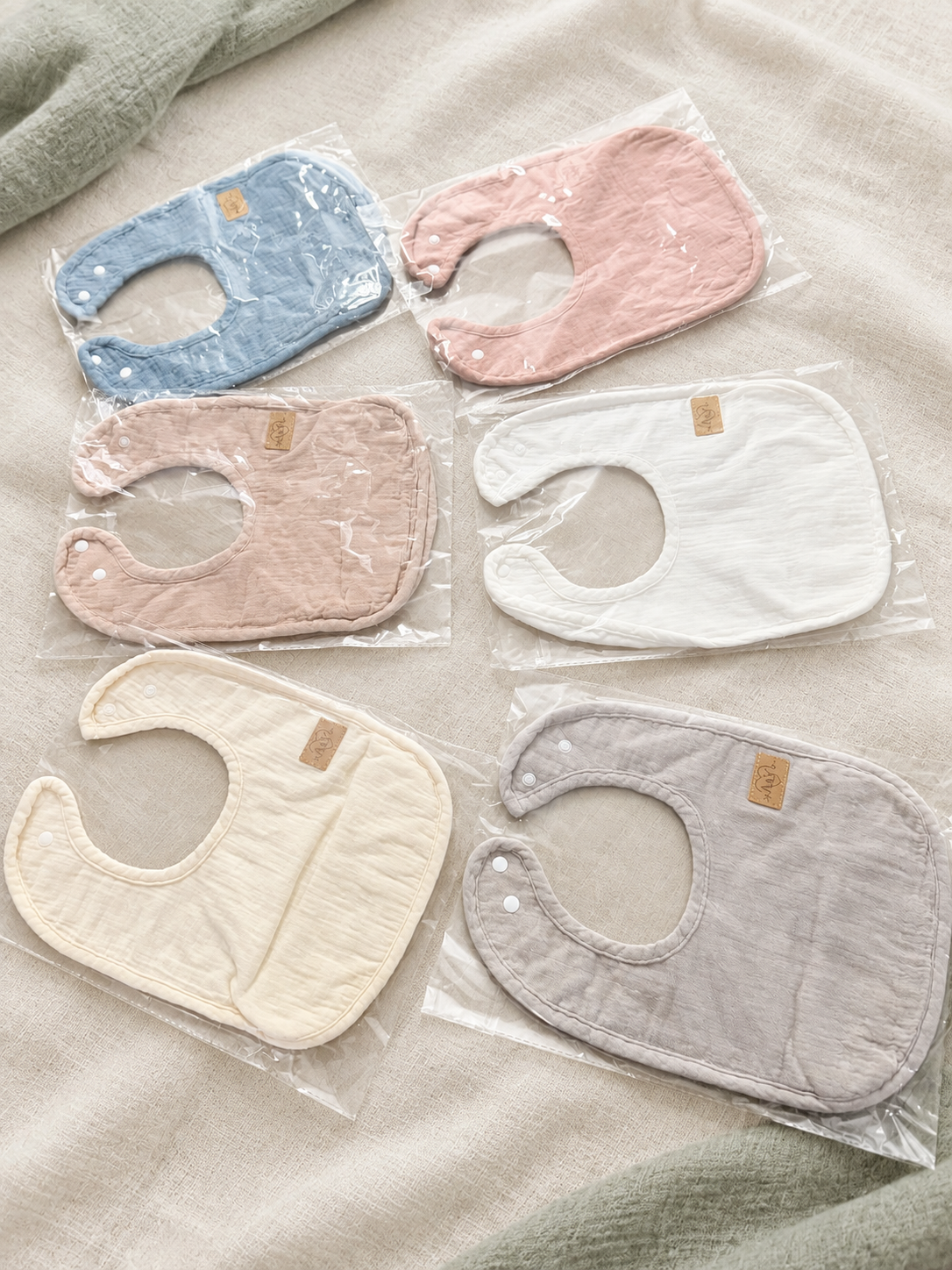 Assortiment de bavoirs MINUS coton et minky dans leurs emballages individuels.