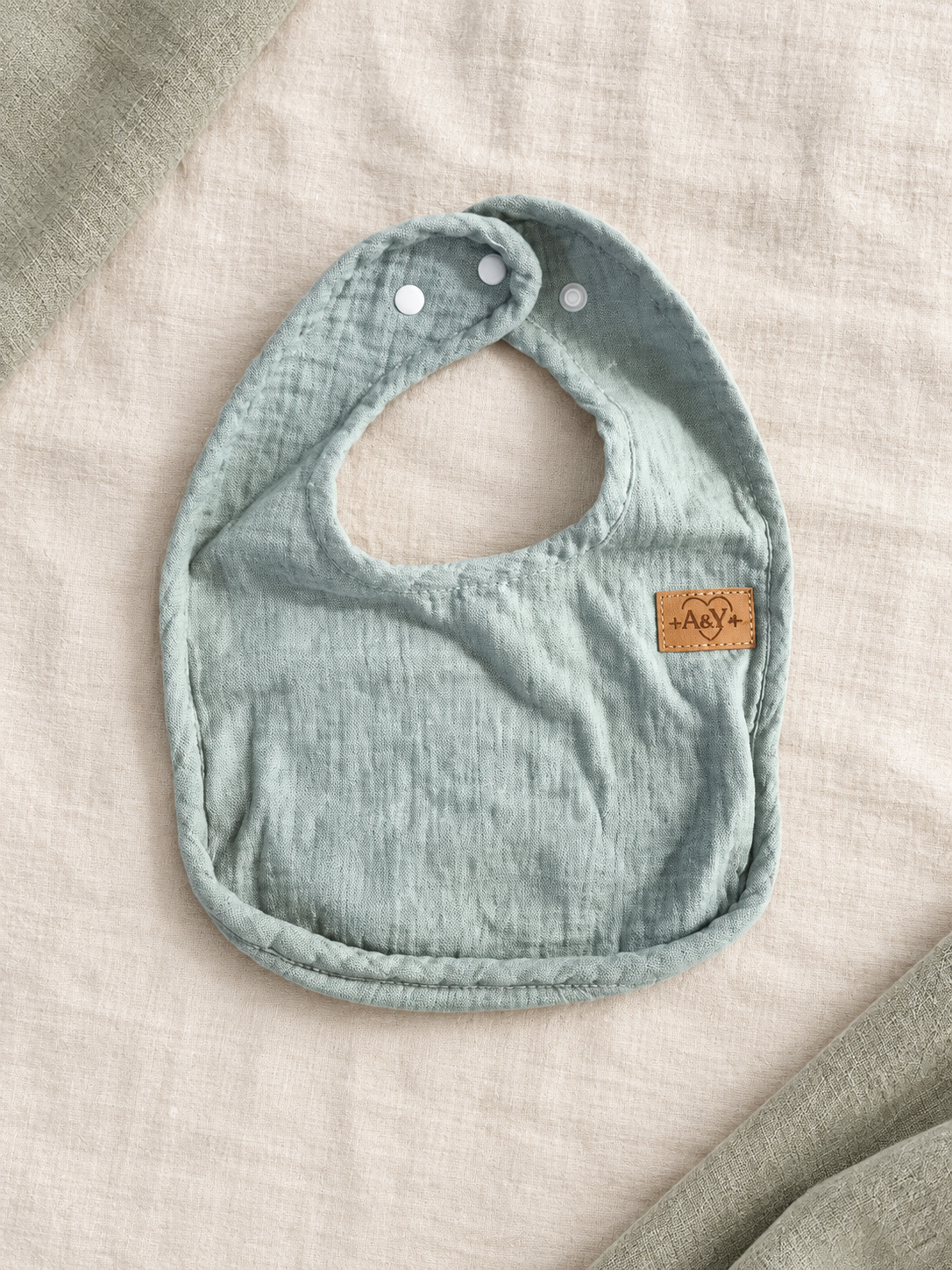 Vue complète du bavoir MINUS sauge avec sa forme arrondie et ses attaches.